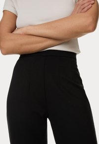 Schwarze hoch taillierte Hose mit glatter Textur, vorne mit Falten, ergänzt durch ein enges, hellgraues Rippoberteil.