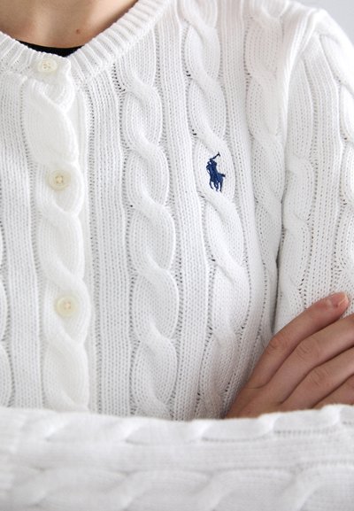 Weißer Strickcardigan mit V-Ausschnitt, gerippten Bündchen, drei Knöpfen und einem kleinen blauen gestickten Logo auf der linken Seite.