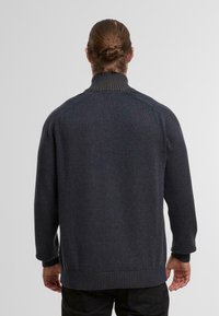 Maglione grigio scuro con colletto alto, polsini e orlo a coste. Presenta un motivo a maglia testurizzato e maniche raglan per facilitare il movimento.