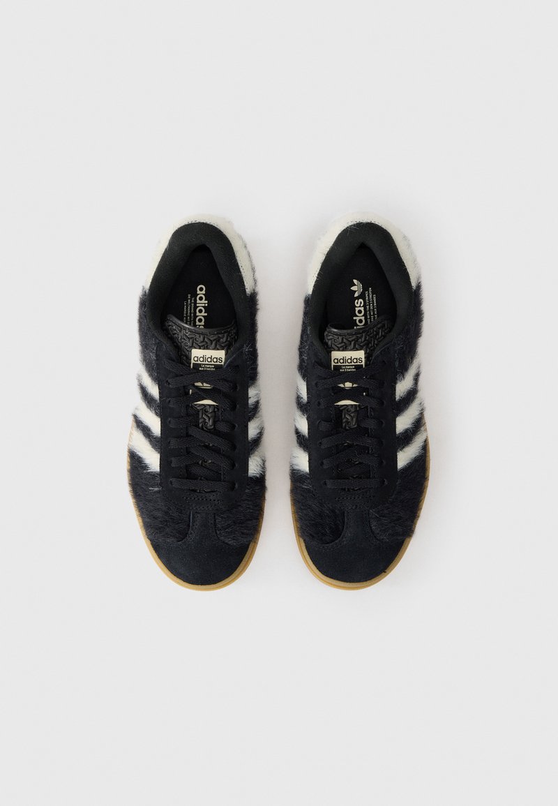 Schwarzer Sneaker mit Felltextur, weißen Streifen und einer Gummisohle. Verfügt über schwarze Schnürsenkel und ein gemustertes Innenfutter.
