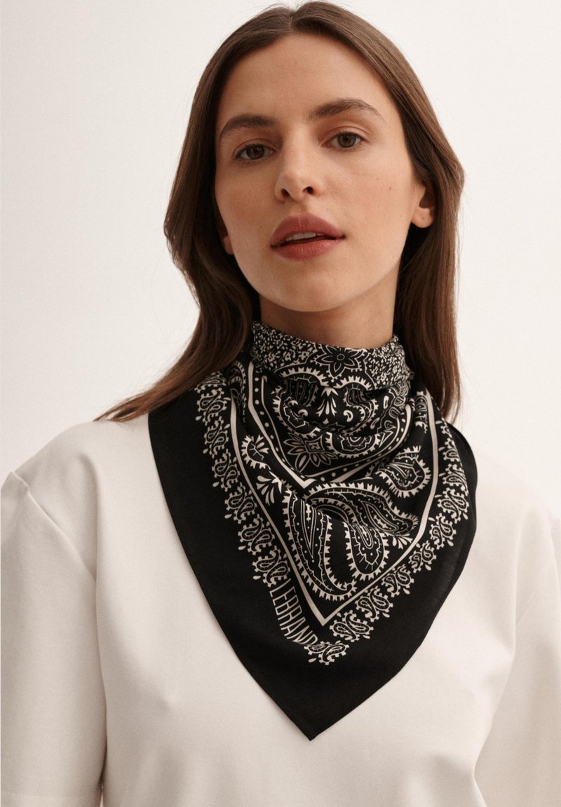 Czarny i biały szal w wzór paisley, wykonany z gładkiego materiału, z ostro zakończonym brzegiem i kontrastowym wykończeniem.