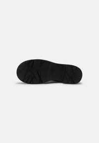 Suela de zapato de goma negra con patrón texturizado, que presenta ranuras y líneas elevadas para una mejor tracción. Forma redondeada, diseño minimalista.