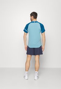 Conjunto atlético para hombre: camisa de manga corta de color azul claro con acentos en azul marino, diseño sin costuras, combinado con pantalones cortos de color azul marino y zapatillas deportivas blancas.