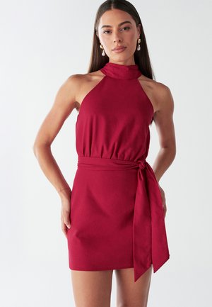 Red halter-neck mini dress in a textured fabric, featuring a knot detail at the waist and a fitted silhouette. Smooth finish.