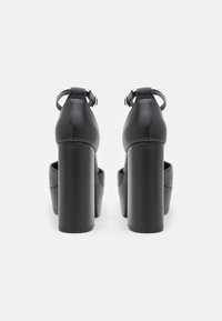 Czarne sandały na wysokim obcasie z grubym blokiem, zamkniętym tyłem, regulowanym paskiem na kostkę oraz gładką skórzaną powierzchnią.