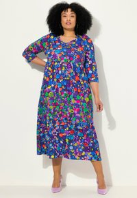 Vestido colorido y estampado con una base azul profunda adornada con diseños florales y circulares multicolores; de largo hasta la rodilla, con mangas de tres cuartos.