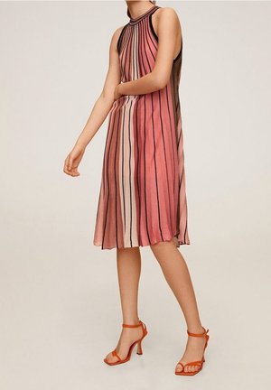 Een mouwloze jurk tot op de knie met verticale strepen in tinten roze en crème, met een zwarte halslijn. Gecombineerd met oranje sandalen met bandjes.