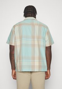 Camicia a maniche corte a scacchi in blu chiaro, beige e crema, con una vestibilità rilassata e un orlo dritto.