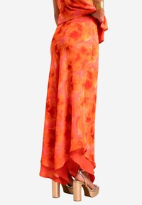 Jupe longue et fluide avec un motif floral vibrant orange et rose. Fabriquée en tissu léger avec un ourlet plus large et un design superposé. Accentuée par des talons compensés dorés.