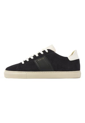 Sort ruskind lavtop sneaker med hvid sål, hvide snørebånd, hvid hælflig og sort læder sidestribe med guldfarvet branding.