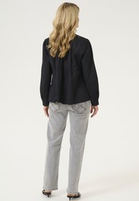 Blusa negra de manga larga con un diseño en capas, combinada con vaqueros rectos grises claros con costuras en contraste y bolsillos traseros.