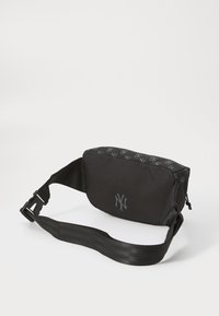 Sac à épaule en tissu noir avec un logo et des accents à motifs. Comprend une fermeture éclair et une sangle réglable pour plus de commodité.
