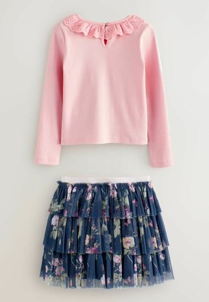 Rosa langærmet skjorte med en blondebesat krave og nøglehulslukning bagpå, parret med en marineblå tylnederdel med blomsterprint og volanter.