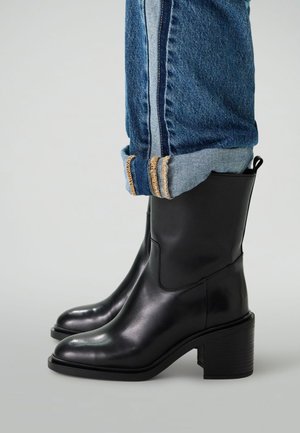 Zwarte leren enkelboots met een blokhak en een ronde neus, gecombineerd met opgerolde denim jeans met contrasterende stiksels.