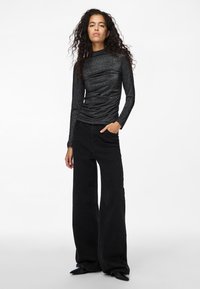 Svart långärmad topp med en texturerad, figurnära design och hög krage. Kombinerad med vida svarta denimjeans och skor med spetsig tå.