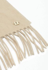 Beżowy wełniany szalik z frędzlami na końcach i małym kwadratowym złotym emblematem przy jednej krawędzi na białym tle.