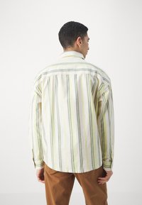Camisa a rayas en amarillo, verde y blanco; tejido ligero, manga larga, cuello abotonado, dobladillo curvado, corte relajado.