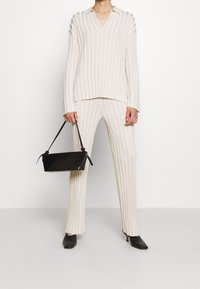 Beige pruhovaný pletený set s topem s véčkovým výstřihem a kalhotami širokého střihu. Černá úzká kabelka s nastavitelnými popruhy. Černé lodičky s špičatou špičkou.