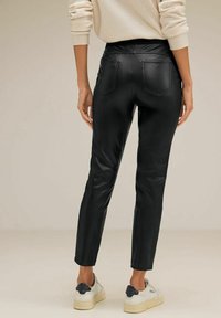 Černé umělé kožené kalhoty s úzkým střihem, zúženými nohavicemi a dvěma zadními kapsami. Nosí se s bílými teniskami a svetrem v neutrální barvě.