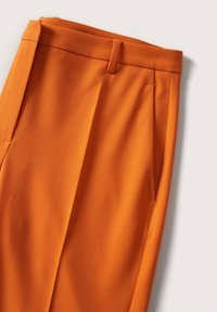 Pantalon orange sur mesure avec passants de ceinture, poches latérales et pli avant, présenté sur un fond clair.