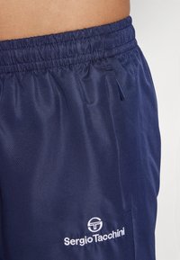Marineblå treningsshorts laget av lett, texturert stoff. Har elastisk midjebånd og hvit logo nederst på siden.