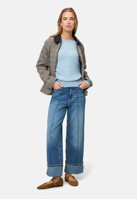 Kurtka w kratę z czarnym kołnierzem, jasnoniebieski sweter, szerokie dżinsy z podwiniętymi mankietami oraz brązowe baleriny.