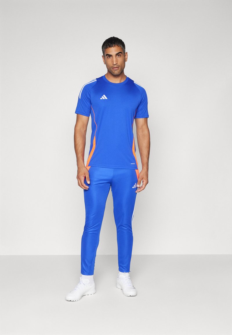 Blaues Sportoberteil und Sporthose mit orangefarbenen Akzenten, aus glattem Material. Mit weißen Streifen an den Schultern und einem Logo auf der Brust und dem Oberschenkel.