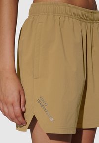 Beige shorts met een elastische tailleband, zijzakken en decoratieve stiksels. Heeft een zilveren print aan de linkerkant onderaan.