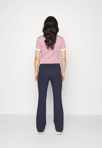 Różowa koszula z krótkim rękawem z białymi wykończeniami, zestawiona z granatowymi spodniami dzwonami. Koszula ma dopasowany krój, natomiast spodnie wykonane są z miękkiego, elastycznego materiału.