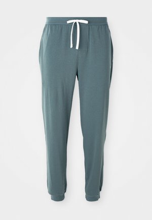 Pantaloni jogger turchesi confortevoli realizzati in tessuto morbido. Dotati di un cordoncino bianco, tasche laterali e caviglie affusolate. Texture liscia con dettagli minimi.