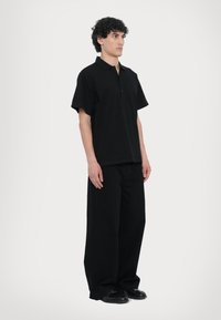Svart polo skjorte med korte ermer og krage, kombinert med svarte vide bukser. Begge plagg laget av et glatt, matt stoff.