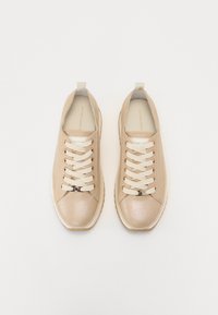 Baskets beige avec une tige texturée, lacets crème et bout rond. Comprend une languette au niveau du talon et une semelle blanche robuste.