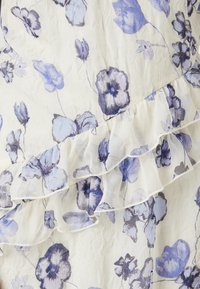 Blomstrete stoff med blå og lilla fiolinger på en lys kremfarget bakgrunn. Har en krøllete hem i gjennomsiktig materiale. Teksturert overflate.