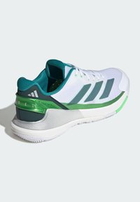 White athletic shoe with green accents, textured mesh upper, three dark stripes, and a grey sole. Notable shiny green detailing on heel.