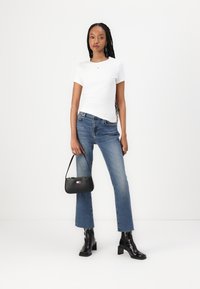 T-shirt bianco attillato, jeans blu a gamba dritta con orlo sfrangiato, stivaletti neri con tacco e una piccola borsa nera con dettagli del logo.
