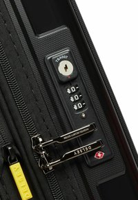 Valigia da viaggio nera con sistema di cerniera bloccabile TSA, superficie texturizzata, doppie cerniere nere con dettagli in argento e una linguetta gialla.