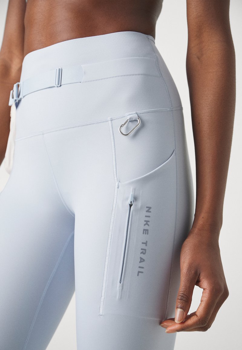 Des leggings de sport bleu clair avec une taille haute, une poche zippée et un accent en boucle en métal. Tissu lisse et extensible avec un détail de logo.