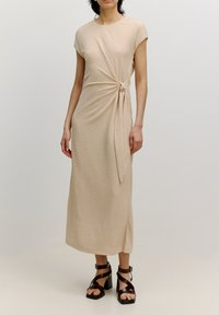 Beiges Midi-Kleid mit einem Knoten-Detail an der Taille. Hergestellt aus einem strukturierten Stoff, mit kurzen Ärmeln und einer geraden Silhouette.