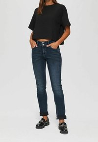 Mustattu lyhythihainen crop-top, yhdistetty tummansiniset slim fit -farkut, joissa on käännetyt hihansuut, ja kiiltävät mustat loaferit.