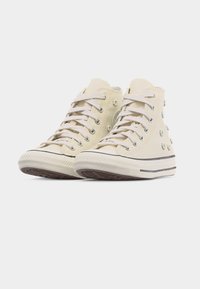 Μπεζ καμβαδένια ψηλά sneakers με κορδόνια, μικρές 3D διακοσμητικές ανθοδέσμες και λευκές λαστιχένιες σόλες με μαύρες ρίγες.