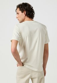 Ljusbeige kortärmad t-shirt i mjukt bomullstyg, med rund halsringning och en slät yta, bärs med beige byxor.