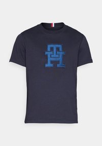 Námořnická modrá polokošile s krátkým rukávem, na hrudi velké vyšívané modré logo "TH" a malý červený, bílý a modrý pruh na výstřihu.