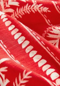 Textil rojo con patrones botánicos blancos, que incluyen líneas curvas y formas de hojas, con una superficie suave y texturizada.