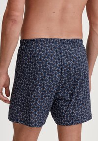 Marineblaue Schwimmshorts mit einem sich wiederholenden geschwungenen Muster in Weiß, Orange und Blau. Verfügt über einen elastischen Bund und eine weiche Stoffoberfläche.