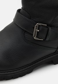 Schwarzer Lederstiefel mit strukturierter Oberfläche, einem auffälligen Riemen mit einer metallischen Schnalle und einer robusten Gummisohle mit Profil.