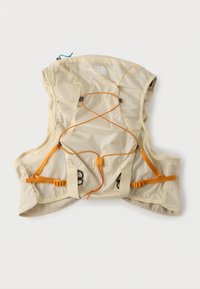 Ανοιχτό μπεζ γιλέκο ενυδάτωσης North Face με πορτοκαλί ρυθμιζόμενους ιμάντες και πλευρικά πάνελ από δίχτυ, σχεδιασμένο για υπαίθριο τρέξιμο ή πεζοπορία.
