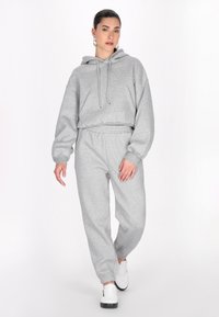 Grå cropped hoodie med snoretræk og kængurulomme, parret med grå joggerbukser med elastisk talje og manchetter, iført hvide sneakers.