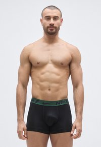 Sorte boxer briefs med en grøn Nike-logo elastik i taljen, lavet af strækbart materiale, med en tætsiddende pasform og glat tekstur.