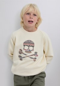 Hanorac de culoare crem, cu un design tip craniu și oase încrucișate, pattern în diverse culori și forme. Guler reiat, mâneci raglan.