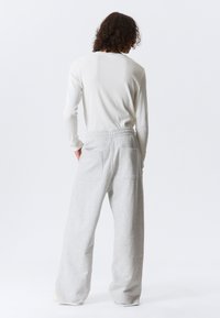 Hellgraue Sweatpants mit lockerer Passform, elastischem Bund und zwei Gesäßtaschen. Der Stoff hat eine weiche, melierte Textur.